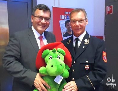 Ein Geschenk von Alfons Weinzierl für Minister Florian Herrmann – ein sogenanntes „Ministerpräsent“: Der grüne Feuerwehrdrache Grisu macht auch g’standenen Politikern Freude.